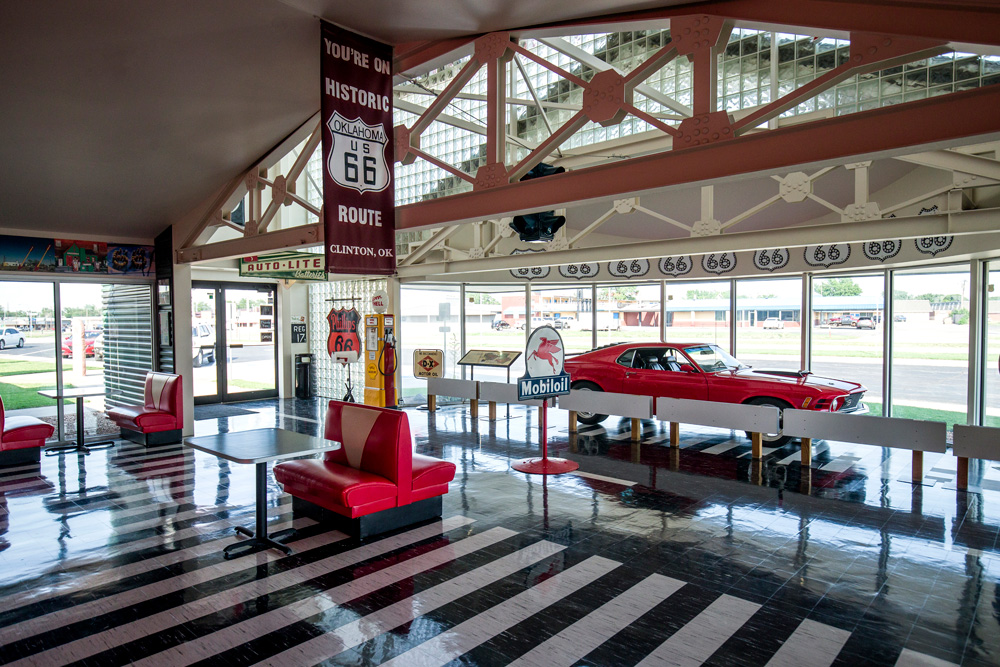 Museum exhibit featuring bright red booths, a red vintage car, and various Route 66 signs