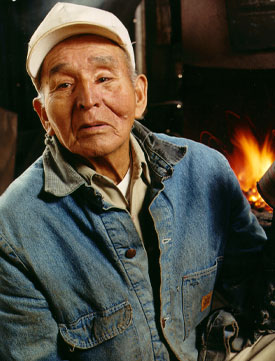 Portrait of Todum Hair at age 84, sitting in front of a blacksmith forge